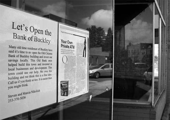 A sign in an empty storefront along Main Street in Buckley encourages grass roots support for re-opening the century-old Bank of Buckley. (PHOTO BY TODD MATTHEWS)