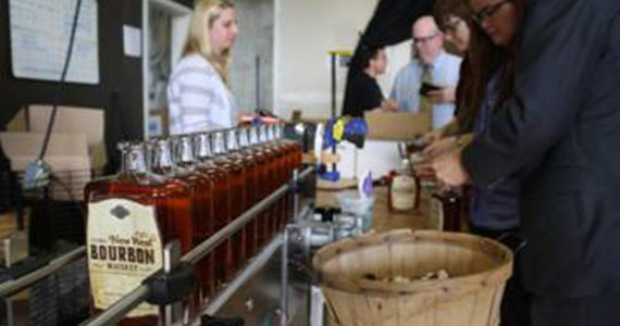 Tacoma Art Museum staff working alongside Heritage Distilling Co.'s crew in Gig Harbor to bottle the final cases of the signature Tacoma New West Bourbon Whiskey, a joint-creation between Heritage Distilling Co. and the Tacoma Art Museum in honor of the November 15 grand opening of the Tacoma Art Museum's Haub Family Collection of Western American Art and museum expansion. (PHOTO BY MYLES LASCO / COURTESY TACOMA ART MUSEUM)