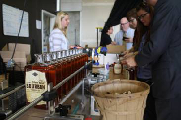 Tacoma Art Museum staff working alongside Heritage Distilling Co.'s crew in Gig Harbor to bottle the final cases of the signature Tacoma New West Bourbon Whiskey, a joint-creation between Heritage Distilling Co. and the Tacoma Art Museum in honor of the November 15 grand opening of the Tacoma Art Museum's Haub Family Collection of Western American Art and museum expansion. (PHOTO BY MYLES LASCO / COURTESY TACOMA ART MUSEUM)