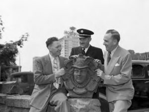 Tacoma Fire Chief Charles Eisenbacher (left) and emergency personnel pose with the 'Head of Mercury' figurehead in 1949. The sculpture was salvaged from the former Fire Station No. 6 in downtown Tacoma, which was built in 1890, damaged during an earthquake in 1949, and demolished in 1974. It is now part of a brick wall that borders a backyard garden at the Mead House. (PHOTO COURTESY SUSAN JOHNSON / ARTIFACTS CONSULTING VIA TACOMA PUBLIC LIBRARY / NORTHWEST ROOM)