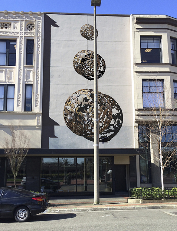 The art installation consists of a trio of three-dimensional metal, laser-cut half-spheres that range in diameter between three feet, five feet, and eight feet, and feature an intricate design pattern. The pieces will be bolted to a blank facade situated between two historic buildings on Broadway. (IMAGE COURTESY JONATHAN CLARREN)