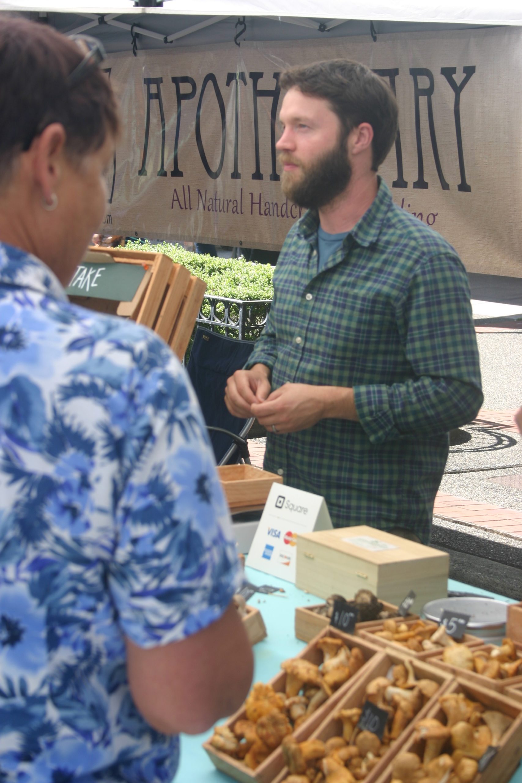 Adam DeLeo, owner of Adam's Mushrooms on the Key Peninsula, speaks with customers about the varieties of farm-grown and wild mushrooms at his booth at the Broadway Farmers' Market in Tacoma, July 15, 2016. Credit: David Guest / TDI
