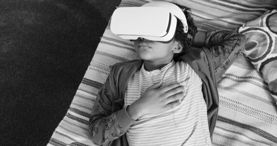 High angle view of African little boy relaxing on sofa and using VR goggles to watch virtual reality video during his leisure time at home