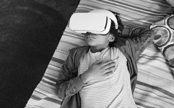 High angle view of African little boy relaxing on sofa and using VR goggles to watch virtual reality video during his leisure time at home