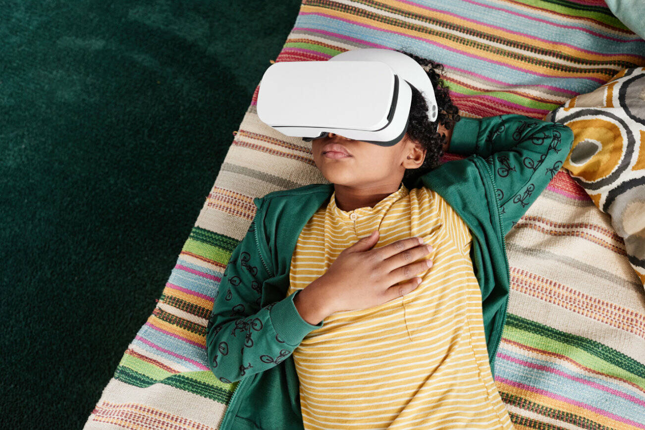 High angle view of African little boy relaxing on sofa and using VR goggles to watch virtual reality video during his leisure time at home