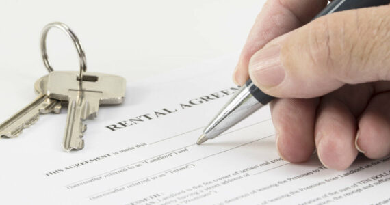 hand is writing with a pen on a rental agreement document, house keys in the background, selected focus, narrow depth of field