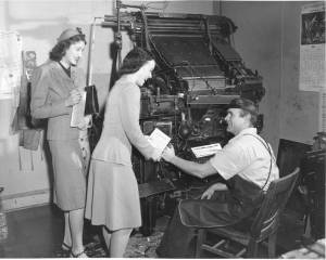 <strong>A Linotype machine is in the background of this image from a 1944 Community War Chest campaign. View of two unidentified War Chest volunteers soliciting funds from an unidentified typesetter. Image courtesy Northwest Room at The Tacoma Public Library, image number: Richards Studio D18294-11</strong>