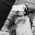 High angle view of African little boy relaxing on sofa and using VR goggles to watch virtual reality video during his leisure time at home