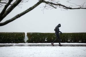 A pedestrian walks through Grand Avenue Park as a light snow comes down Tuesday, Feb. 28, 2023, in Everett, Washington. (Ryan Berry / The Herald)