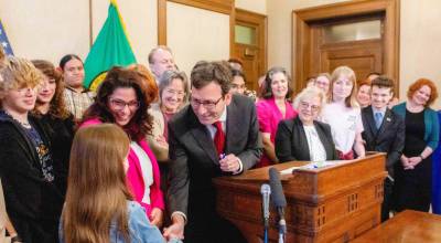 Gov. Bob Ferguson hands over one of the pens he used to sign House Bill 1296, the students bill of rights to a child who attended the bill signing. (Photo by Jacquelyn Jimenez Romero/Washington State Standard)